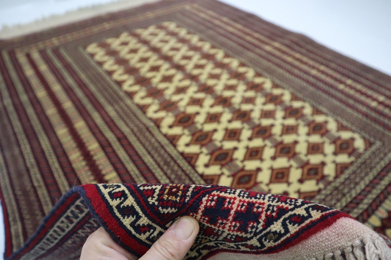 May include: A traditional hand-woven rug with a geometric pattern in shades of red, brown, beige, and cream. The rug has a fringe border and is made of wool.