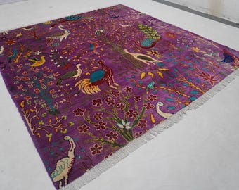 May include: A vibrant purple rug with a tree of life design, featuring colorful birds and floral elements. The rug has a fringed edge and is likely made of wool or a similar material. The design includes peacocks, roosters, and other birds.