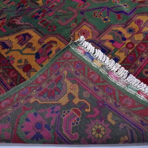 May include: A close-up of a colourful rug with intricate patterns in shades of green, pink, yellow, and blue. The rug has a fringed border and is made of a soft, woven material.