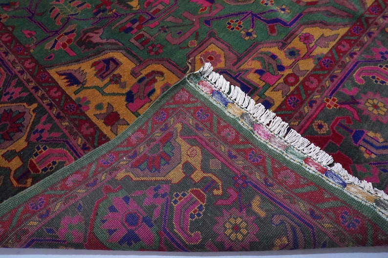 May include: A close-up of a colourful rug with intricate patterns in shades of green, pink, yellow, and blue. The rug has a fringed border and is made of a soft, woven material.