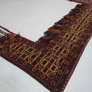 May include: A burgundy and gold geometric patterned rug with tassels. The rug features a repeating diamond and square design in shades of burgundy, gold, and black. The edges are finished with tassels in various colors.