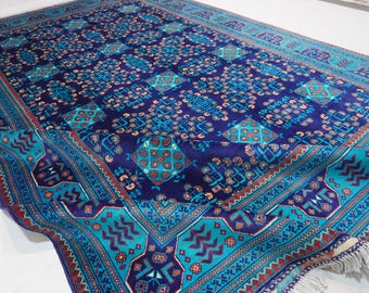 May include: A large rectangular area rug featuring a deep navy blue background with a repeating pattern of turquoise geometric diamonds and floral motifs. The border displays a vibrant turquoise band with red and dark purple accents and fringe.