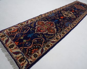 May include: A long, narrow rug with a navy blue background and intricate floral patterns in shades of red, orange, and cream. The rug has a fringe on both ends.