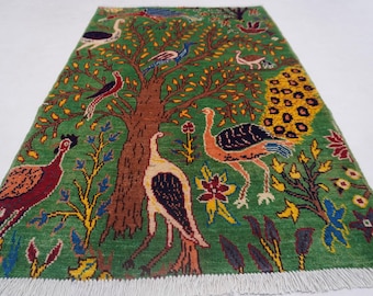 May include: A rectangular green rug with a tree and bird design. The rug features a brown tree trunk with green leaves, and various birds in red, blue, and white. The rug has a white fringe.