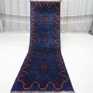 May include: A blue and red runner rug with a geometric pattern. The rug has a fringe border.