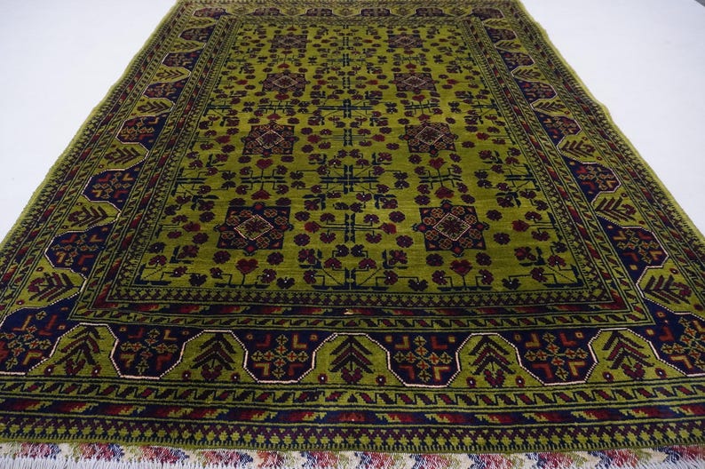 May include: A green rug with a geometric pattern in shades of red, blue, and green. The rug has a fringe border.