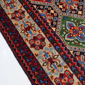 May include: A close-up of a colourful rug with intricate geometric patterns in shades of red, blue, green, and beige. The rug has a border with a floral design.