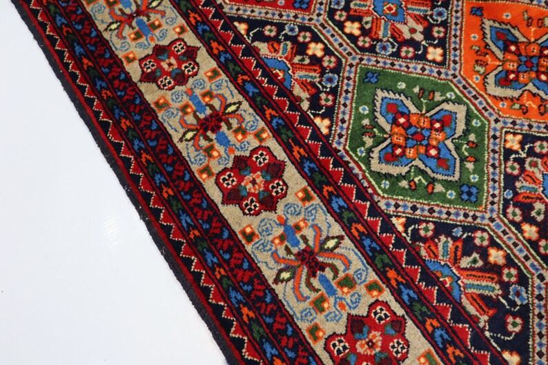 May include: A close-up of a colourful rug with intricate geometric patterns in shades of red, blue, green, and beige. The rug has a border with a floral design.