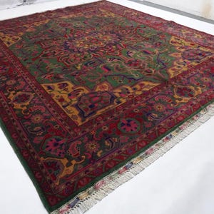 May include: A large, intricately patterned rug with a green, red, and gold colour scheme. The rug has a fringe border and features a central medallion with floral and geometric designs.