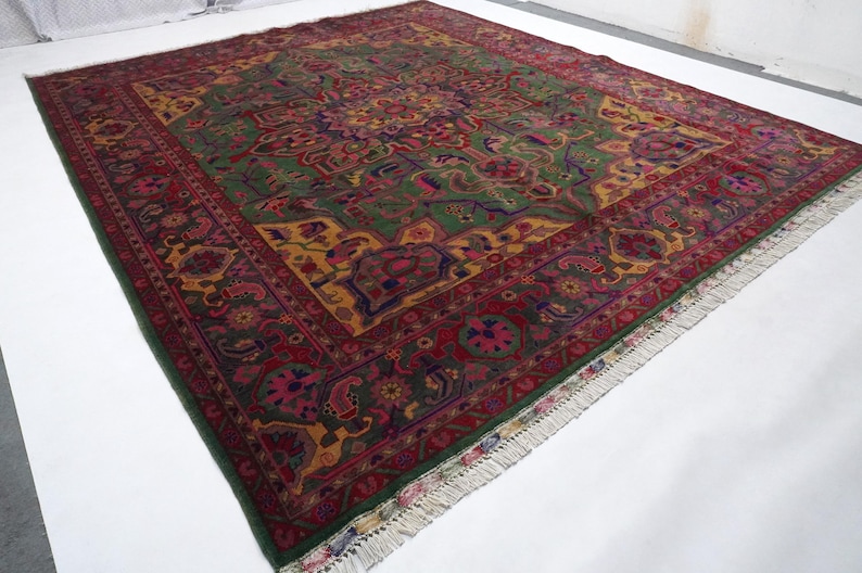 May include: A large, intricately patterned rug with a green, red, and gold colour scheme. The rug has a fringe border and features a central medallion with floral and geometric designs.