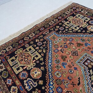May include: A traditional Persian rug with a black background and intricate patterns in shades of red, blue, and gold. The rug has a fringe border and features a central diamond-shaped design.