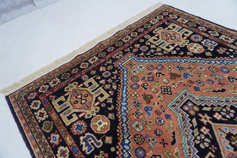 May include: A traditional Persian rug with a black background and intricate patterns in shades of red, blue, and gold. The rug has a fringe border and features a central diamond-shaped design.