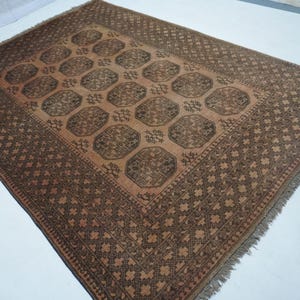 May include: A rectangular, brown area rug with a central pattern of repeating octagons and a detailed border. The rug has a fringe along the edges and is made of woven material.