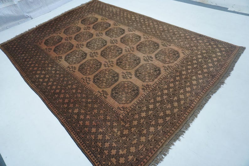 May include: A rectangular, brown area rug with a central pattern of repeating octagons and a detailed border. The rug has a fringe along the edges and is made of woven material.