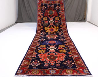 May include: A long, narrow rug with a dark blue background and intricate floral patterns in shades of red, yellow, and orange. The rug has a fringe border.