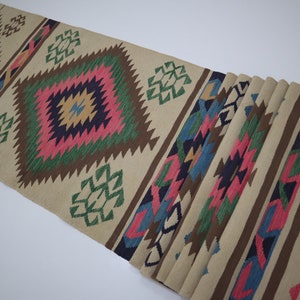 May include: Beige runner rug with geometric patterns in pink, green, blue, and brown. The rug features diamond and zigzag designs, with a fringed edge. Ideal for adding a touch of color and texture to any space.