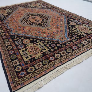 May include: A traditional Persian rug with a black background and intricate patterns in shades of red, orange, blue, and green. The rug has a fringe border.