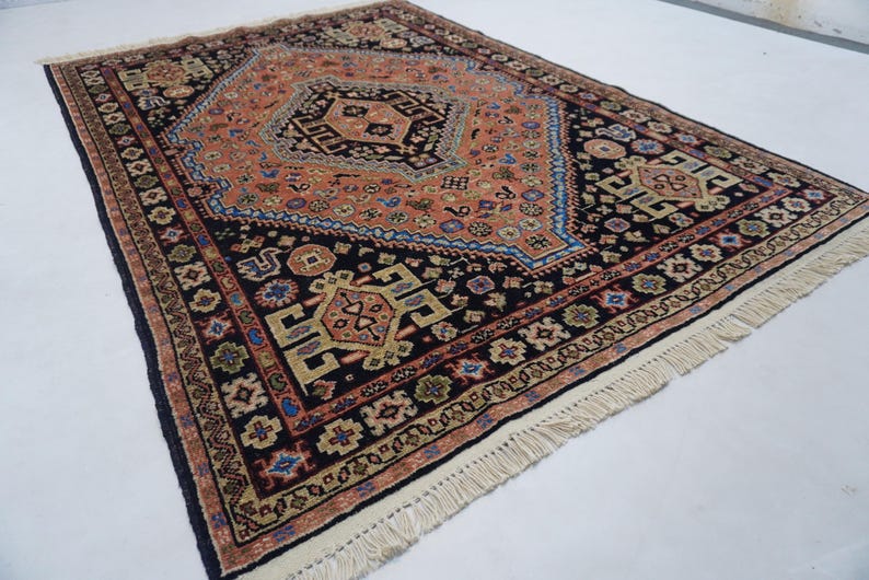 May include: A traditional Persian rug with a black background and intricate patterns in shades of red, orange, blue, and green. The rug has a fringe border.