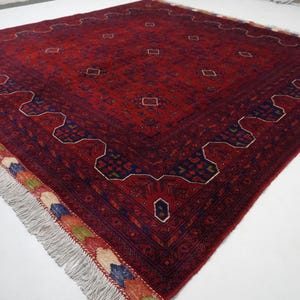 Pu&ograve; includere: Un tappeto rosso, blu e crema con un motivo geometrico e frange. Il tappeto ha un design tradizionale ed &egrave; fatto di lana.