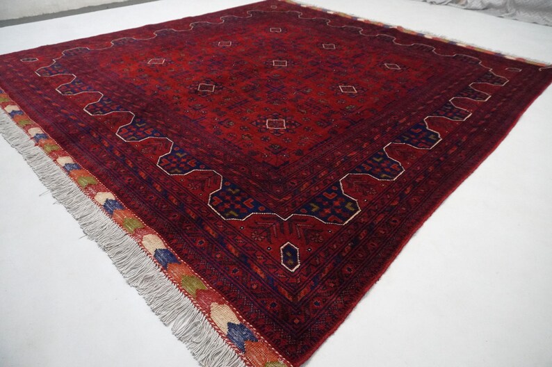 Pu&ograve; includere: Un tappeto rosso, blu e crema con un motivo geometrico e frange. Il tappeto ha un design tradizionale ed &egrave; fatto di lana.