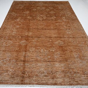 May include: A rectangular, brown rug with a detailed pattern. The rug has a textured appearance and a fringe along the bottom edge. The design features floral and geometric elements in a lighter shade of brown.