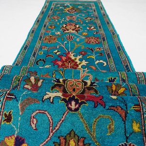 May include: A teal blue runner rug with a floral pattern in shades of red, yellow, and green. The rug has a border with a geometric design.