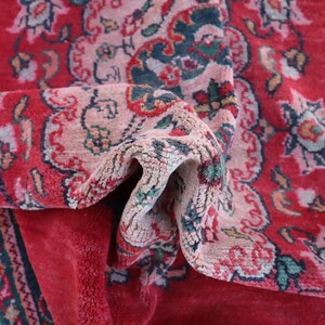 May include: A close-up of a red rug with a floral pattern. The rug is folded in half, revealing the intricate details of the design. The rug is made of a soft, plush material.
