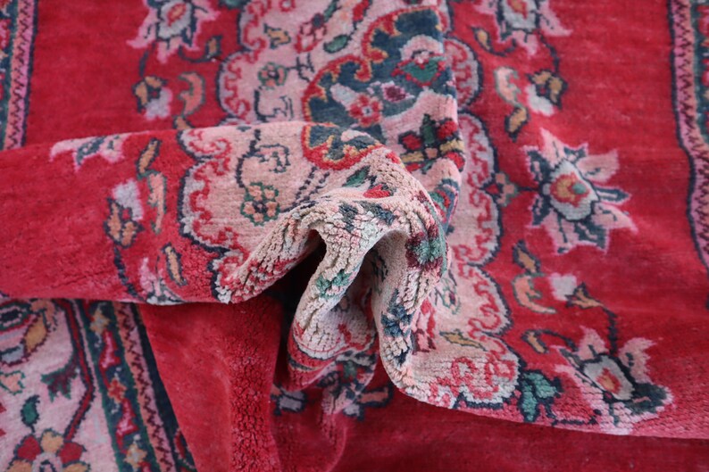 May include: A close-up of a red rug with a floral pattern. The rug is folded in half, revealing the intricate details of the design. The rug is made of a soft, plush material.