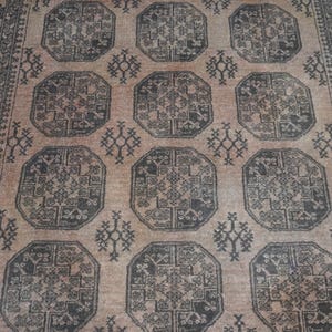May include: A beige and black patterned rug with a repeating geometric design. The rug features a central field of octagonal shapes with intricate details, surrounded by a border with a similar pattern. The rug's color palette is neutral, with shades of beige and black.
