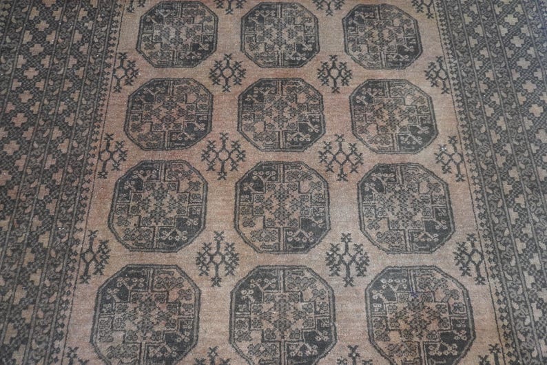 May include: A beige and black patterned rug with a repeating geometric design. The rug features a central field of octagonal shapes with intricate details, surrounded by a border with a similar pattern. The rug's color palette is neutral, with shades of beige and black.
