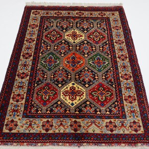 May include: A traditional Persian rug with a dark blue background and a geometric pattern of red, green, and yellow. The rug has a cream-coloured border with intricate floral designs.
