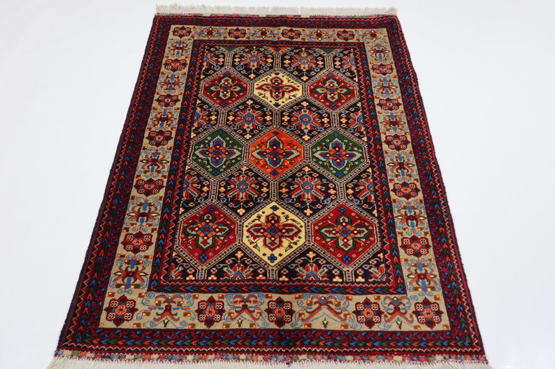 May include: A traditional Persian rug with a dark blue background and a geometric pattern of red, green, and yellow. The rug has a cream-coloured border with intricate floral designs.