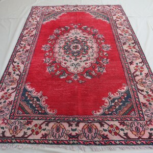 May include: A red rug with a floral pattern and a central medallion. The rug has a dark blue border with a pink and white inner border.