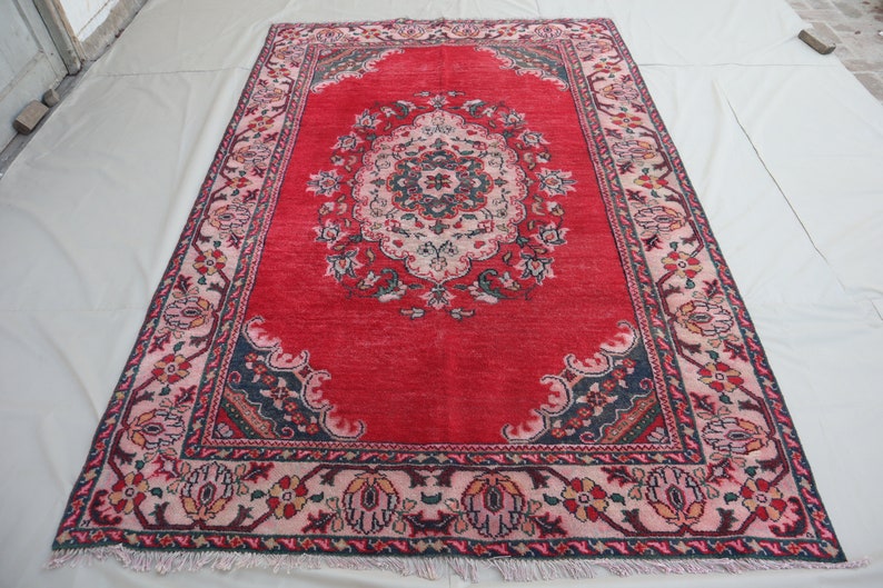 May include: A red rug with a floral pattern and a central medallion. The rug has a dark blue border with a pink and white inner border.