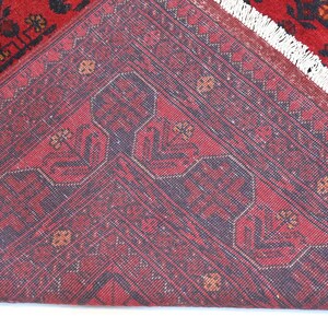 May include: Close-up of the back of a red rug with a dark blue geometric pattern. The rug has a white fringe.
