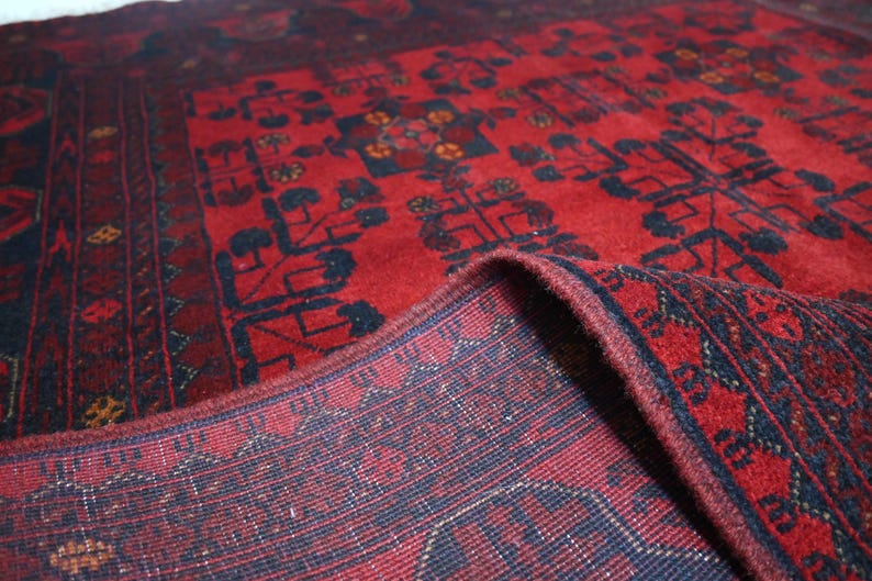 May include: A red and blue rug with a traditional Persian design. The rug is folded in half, showing the intricate details of the weave.