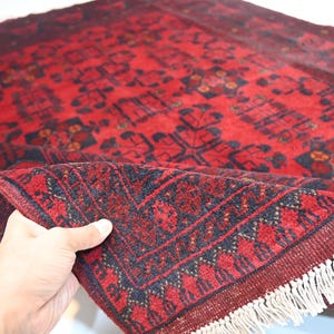 May include: A red and black hand-woven rug with a traditional Persian design. The rug has a fringe border and is folded in half.