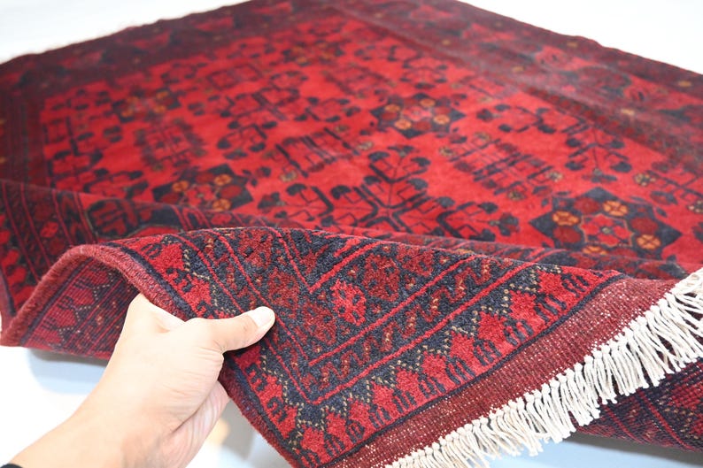 May include: A red and black hand-woven rug with a traditional Persian design. The rug has a fringe border and is folded in half.