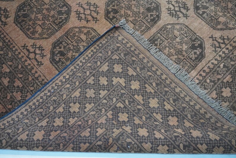 May include: Close-up of a brown and black patterned rug. The rug features geometric designs and a detailed border. The corner of the rug is folded back, revealing the underside with a contrasting pattern. The rug has a fringe along one edge.