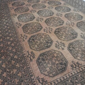 May include: A vintage rug with a central pattern of dark brown octagons and floral motifs on a light brown background. The rug has a dark brown border with geometric designs. The overall aesthetic is rustic and traditional.