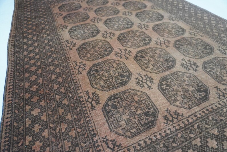 May include: A vintage rug with a central pattern of dark brown octagons and floral motifs on a light brown background. The rug has a dark brown border with geometric designs. The overall aesthetic is rustic and traditional.