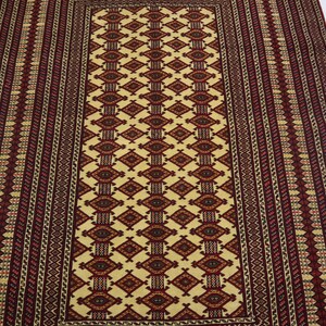 May include: A traditional rug with a cream background and intricate red, black, and yellow geometric patterns. The rug has a rectangular shape and a fringed edge.