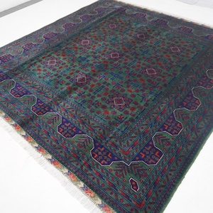 May include: A rectangular, hand-woven rug with a green and blue central field. The rug features a repeating geometric pattern in red and blue, with a detailed border. The edges have a fringe.
