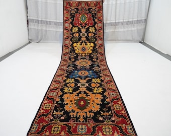 May include: A long, narrow runner rug with a black background and intricate floral patterns in shades of red, orange, yellow, blue, and green. The rug has a traditional Persian design.