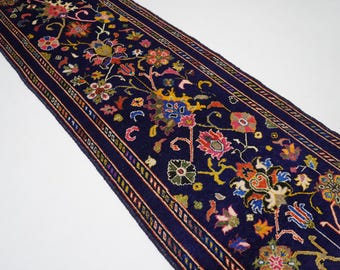 May include: A long, narrow rug with a dark blue background and a colorful floral pattern. The rug has a border with a repeating pattern of small, colorful shapes.