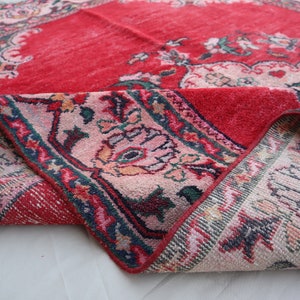 May include: A red and pink rug with a floral pattern. The rug is folded in half, showing the back side, which is a cream colour with a floral pattern.