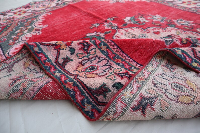May include: A red and pink rug with a floral pattern. The rug is folded in half, showing the back side, which is a cream colour with a floral pattern.
