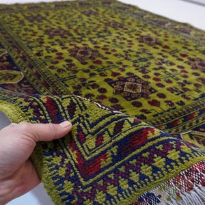 May include: A green, red, and blue patterned rug with fringe. The rug has a geometric design and is folded in half.