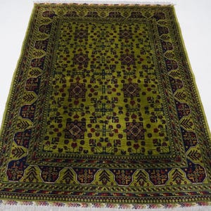 May include: A green rug with a dark red and black geometric pattern. The rug has a fringe border.