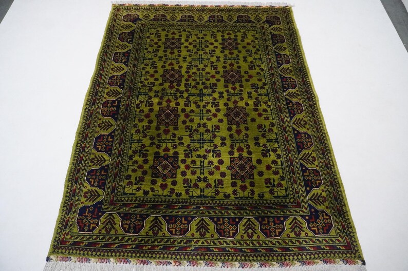 May include: A green rug with a dark red and black geometric pattern. The rug has a fringe border.
